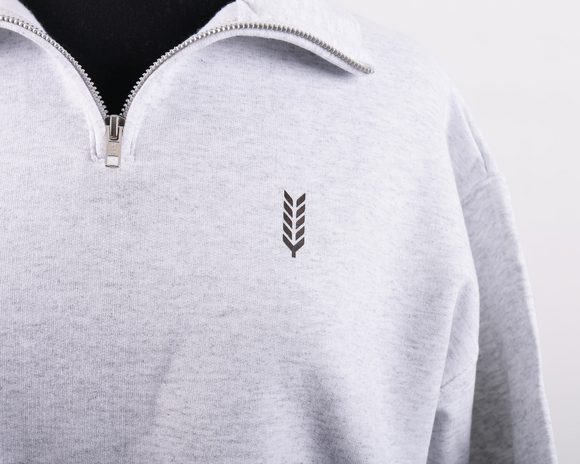 Close up of a grey quarter zip with a silver zipper and small brown wheat illustration on the left breast. 