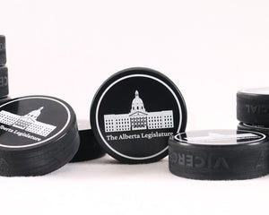 A collectible black hockey puck featuring a white graphic of the Alberta Legislature building. A perfect Canadian souvenir for hockey fans and history lovers.