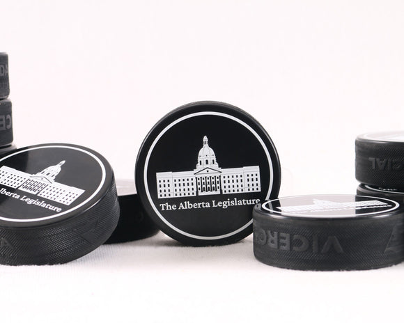 A collectible black hockey puck featuring a white graphic of the Alberta Legislature building. A perfect Canadian souvenir for hockey fans and history lovers.