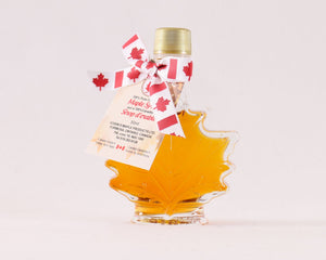 A maple leaf shaped bottle with amber coloured maple syrup inside. 