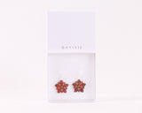 A pair of red flower-shaped earrings with intricate cut-out patterns, displayed in a white box labeled "OHTSII."