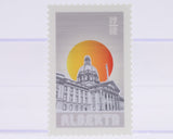 Stamp with a building design crowned by a brought yellow and orange sun and 'Alberta' text on a white background